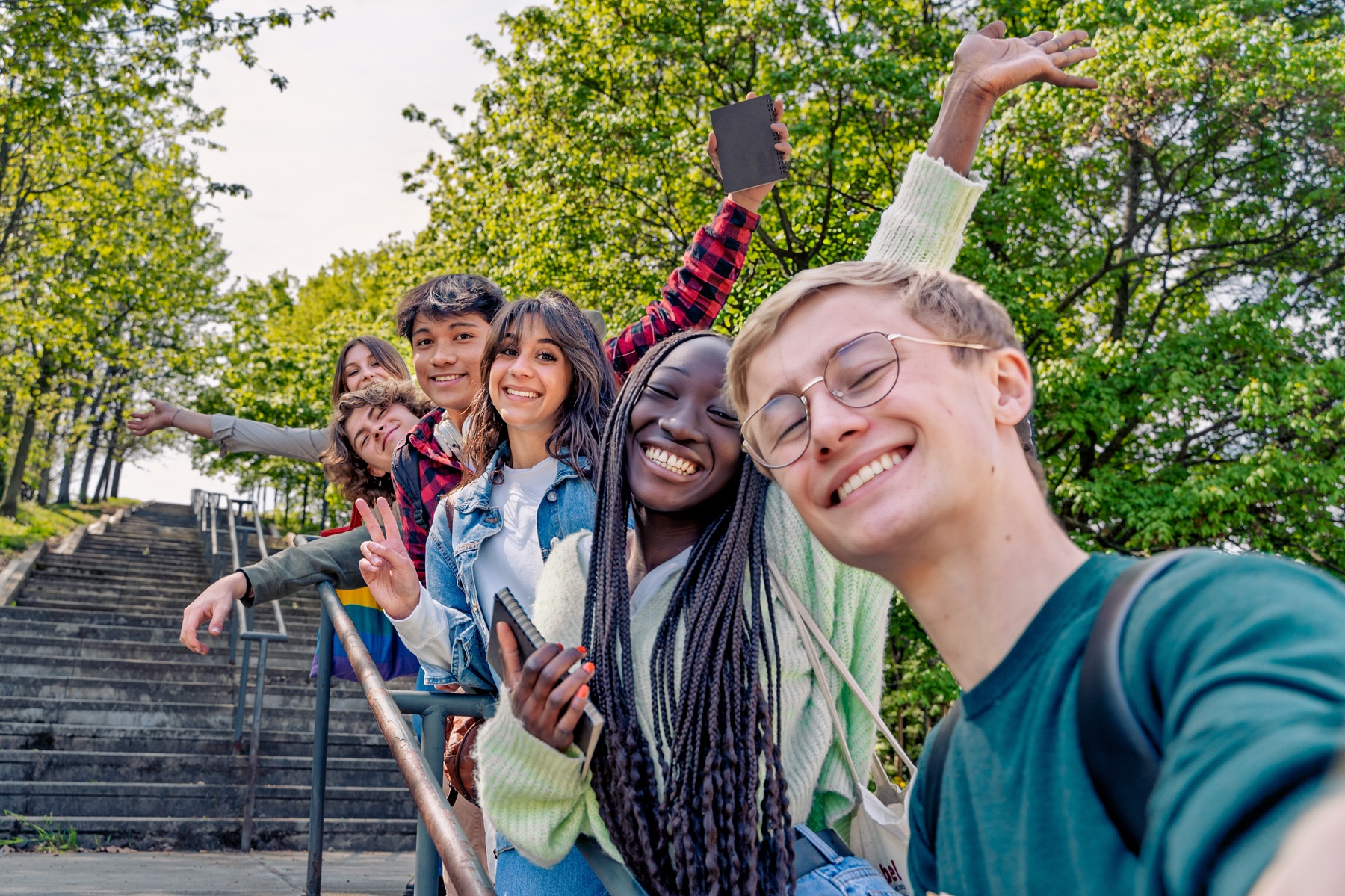 A diverse group of students taking a selfie outdoors, smiling and having fun in a natural environment.